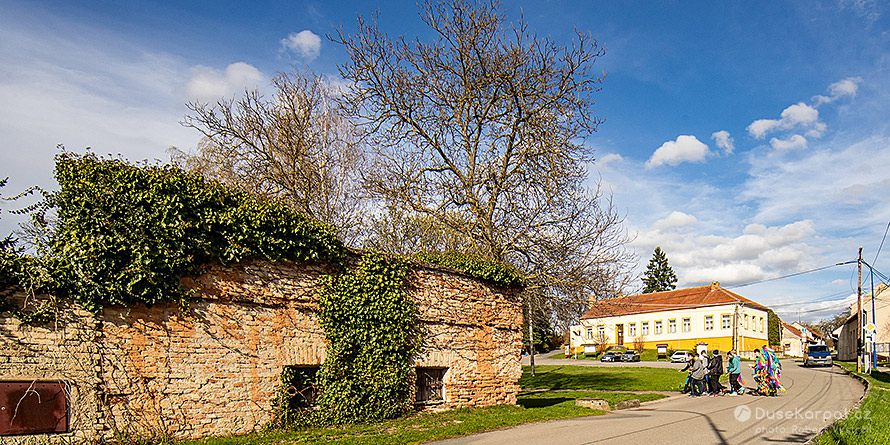 Velikonoční průvod s Jidášem prochází centrem Kojátek, vlevo pozůstatek původní zámecké zdi